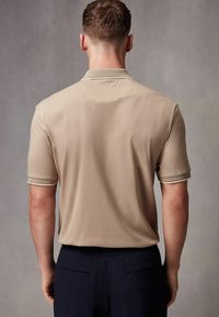 Beige-paita, jossa on lyhyet hihat, teksturoitu kaulus ja hihansuut. Tasainen pinta, istuva malli, yhdistetty tummiin housuihin.