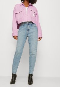 Violetti lyhyt farkkutakki, jossa on kaksi etutaskua, yhdistettynä vaaleansinisiin korkeavyötäröisiin farkkuihin ja mustiin kärkitossuihin.