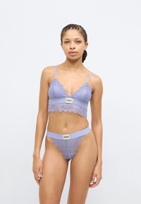 Lavendli pitsist rinnahoidja ja sobiv tangapüks, millel on lainelised servad ja bränditud riba. Kangas on õrn ja struktuurne.