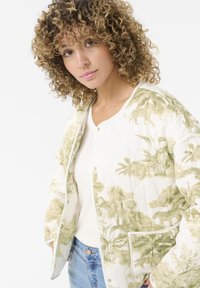 Blouson matelassé blanc avec des motifs de feuillage tropical et d'animaux verts. Doté de boutons pression et de poches latérales. Texture de tissu douce.