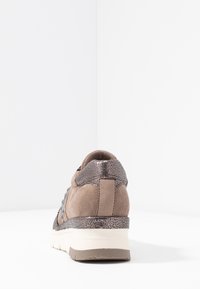 Bruna mockaskor med metalliska accenter, struktur på hälen, vit sula och låg klippdesign. Har en slät, böjd form.