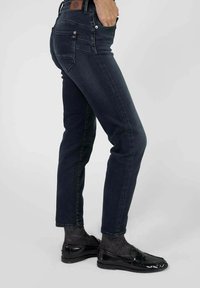 Jean foncé avec une coupe slim, en toile de denim, décoloration subtile, cinq poches et une étiquette en cuir de marque à la taille. Associé à des mocassins noirs brillants.