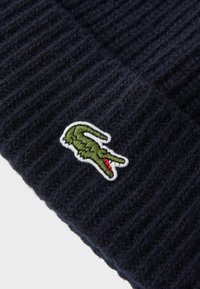 Mornarško modra rebrasta pletena kapa z izvezenim zelenim krokodilom na sprednji strani in belim robom okoli logotipa.