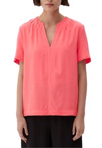 Blouse à manches courtes et col en V de couleur corail vif, réalisée en tissu lisse avec de subtils plis au niveau de l'encolure. Coupe droite et coupe décontractée.