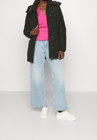 Svart kviltad pufferjacka med huva, i kombination med en rosa v-ringad topp och ljusblå vida jeans, fulländad med vita sneakers.