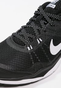 Mustat urheilusandaalit, joissa on verkkomateriaali ylhäällä, teksturoidut pinnat ja valkoinen Nike-logoelementti. Musta-valkoiset kirjavarakenteiset nauhat, pehmustettu pohja.