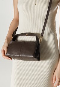 Brązowa skórzana torebka o teksturowanej powierzchni, z krótkim uchwytem i odpinanym paskiem. Posiada złote akcenty hardware.
