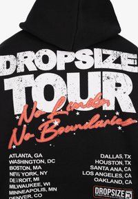 Hoodie noir avec un grand texte blanc "DROPSIZE TOUR", une inscription orange "No Limits No Boundaries" et une liste de villes américaines au dos.