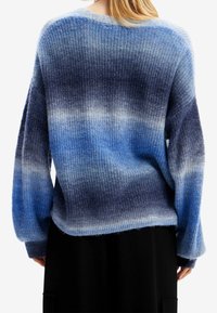 Blå gradiente tröja med ribbad textur, med långa ärmar och en lös passform. Färgen övergår från ljusblått till mörkblått.