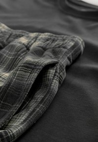 Czarna tkanina T-shirt z gładką teksturą obok szarej i czarno-szarej tkaniny w kratę, charakteryzującej się miękką, flanelową teksturą i widocznymi szwami.