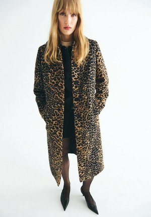 Dlhý kabát v leopardom vzore s jemnou textúrou, so štandardným strihom a gombíkmi pozdĺž prednej časti. Nosený cez čierny outfit a lodičky.