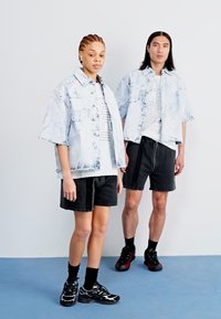 To modeller iført matchende lys blå marmorert denimjakker over hvite t-skjorter med grafikk, kombinert med svarte shorts og joggesko.