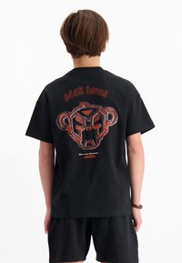 Zwarte katoenen t-shirt met een grafisch ontwerp van een berenachtige gezicht in rood en wit op de achterkant, korte mouwen en een relaxte pasvorm.