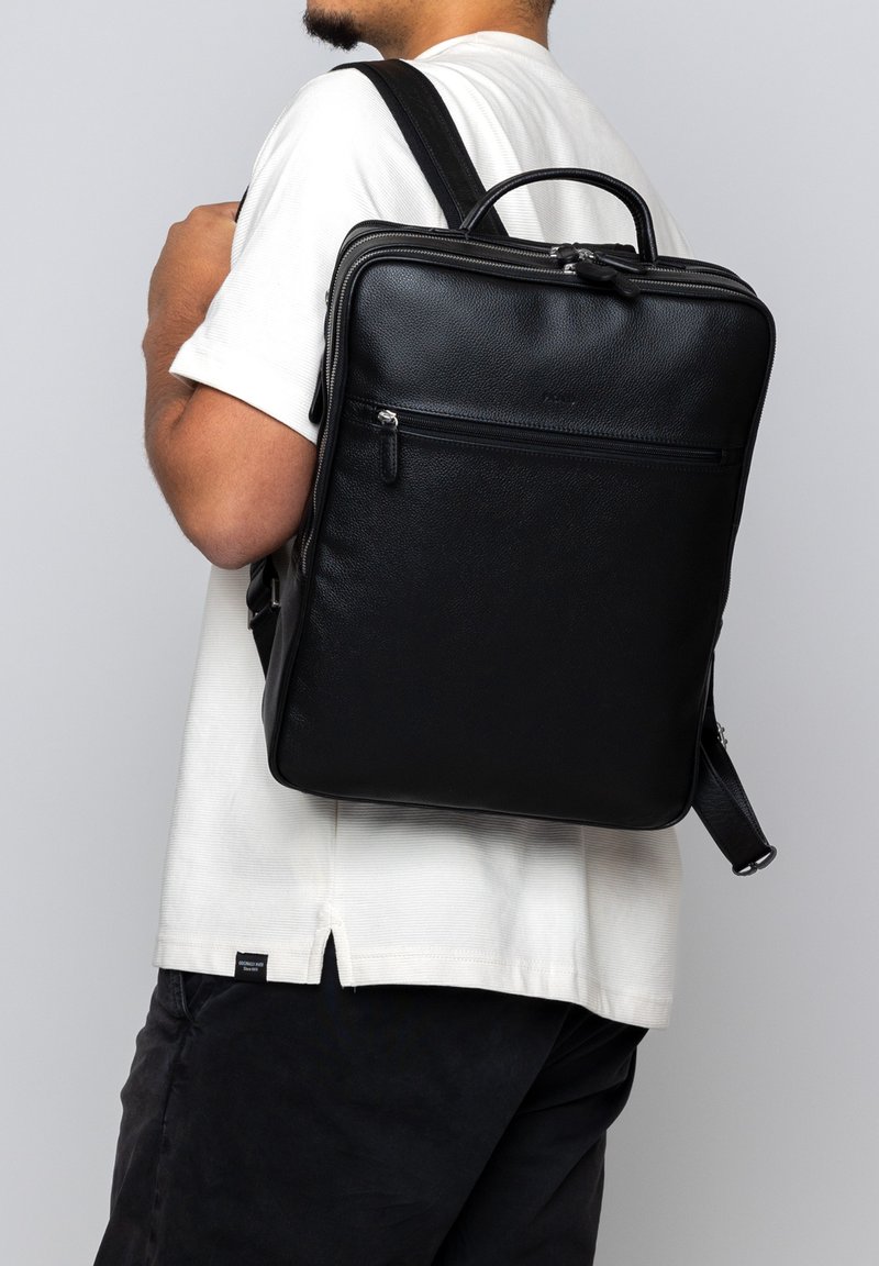 Sac à dos en cuir noir avec une finition texturée, compartiments à double zip et une poignée supérieure. Sangles ajustables pour une polyvalence de transport.