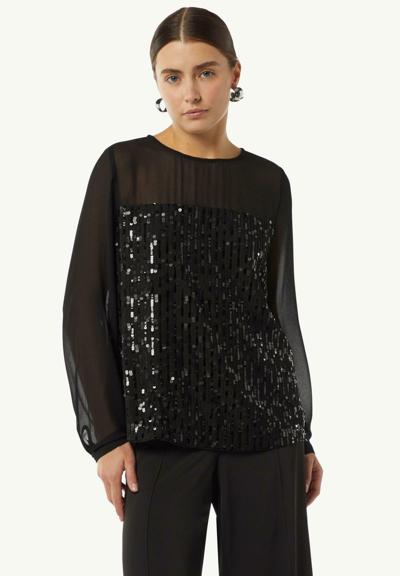 Schwarze Bluse aus transparentem Stoff, mit langen Ärmeln und einem Vorderteil, das mit Pailletten verziert ist. Weicher Stoff mit relaxed Fit.