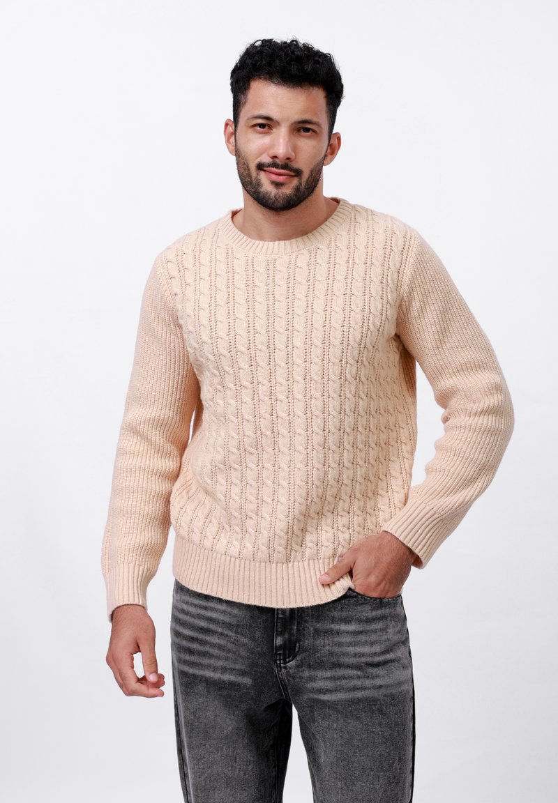 Pull en tricot pêche avec un motif en relief, des poignets et un ourlet côtelés. Porté avec un jean gris, mettant en valeur les détails de texture et de motifs.