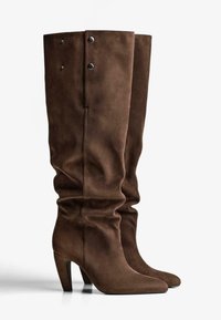 Brązowe zamszowe kozaki sięgające do kolan o luźnym kroju i spiczastych noskach, z okrągłymi srebrnymi guzikami na górnej części.