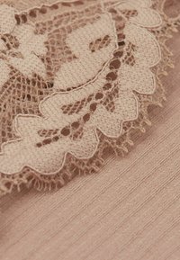 Lichtroze stof met ingewikkelde kantafwerking met gegolfde randen en delicate bloemmotieven, in contrast met een gladde, textuurrijke achtergrond.