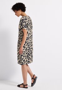 Robe imprimée léopard en beige et noir, à manches courtes, coupe décontractée, longueur genoux, tissu doux, accompagnée de sandales noires.