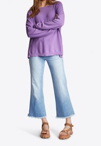 Fioletowa bluzka z długim rękawem połączona z jasnoniebieskimi dzwonami i brązowymi sandałami na platformie z paskami na kostce. Teksturowana tkanina i strzępione krawędzie.