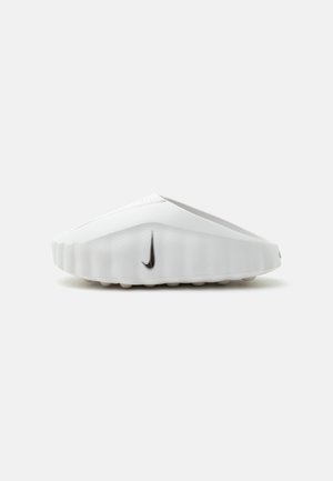 Biela sandála typu slip-on s textúrovanou, rebrovanou podrážkou a čiernym logom Nike na boku, na jednoduchom pozadí.