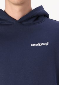 Felpa blu navy realizzata in morbido tessuto, con tasca frontale e logo ricamato bianco sul petto. Il cappuccio ha i cordini regolabili.