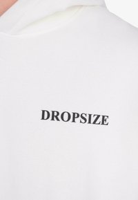 Weißer Hoodie mit schwarzem, großgeschriebenem "DROPSIZE"-Text, der auf der Brust nahe dem Halskragen aufgedruckt ist.