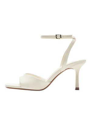 Krémfehér magas sarkú szandál nyitott orral, csatos bokapánttal és vékony, kúpos sarokkal, fehér háttéren.