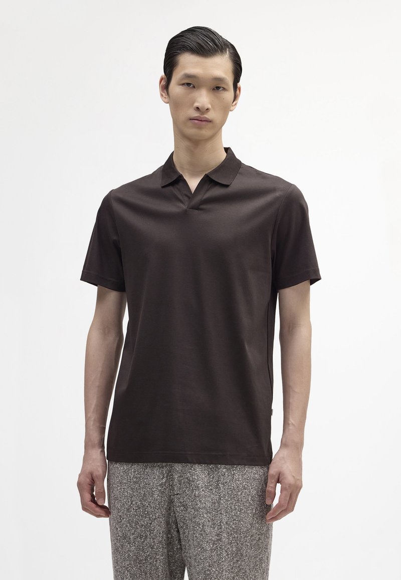 Brązowa koszulka polo z krótkim rękawem, z kołnierzykiem i subtelny połyskiem. Noszona z teksturowanymi szarymi spodniami o luźnym kroju i bocznymi rozcięciami.