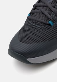 Mørkegrå sportssko med en struktureret mesh-overdel, der har blå snørebånd og en grå sål. Glat design med rund tå og minimalt pynt.