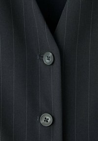 Veste de costume à fines rayures sombre avec deux boutons noirs attachés sur la fermeture avant.