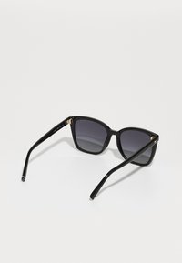 Lunettes de soleil noires carrées avec des verres gris dégradés, monture en plastique, branches fines noires et accents en or près des charnières.