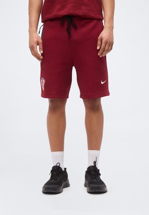 Mężczyzna noszący bordowe szorty sportowe z chorwackim emblematem i białym logo Nike, w połączeniu z białymi skarpetami i czarnymi butami sportowymi.