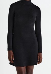 Abito nero a maglia con colletto alto, maniche lunghe e una silhouette aderente. Presenta un tessuto testurizzato e un orlo leggermente svasato.