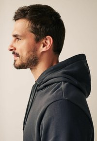 Sweat à capuche gris avec cordon de serrage, doté d'une poche kangourou et d'une coupe décontractée. Texture lisse et design de capuche ajustable bien visibles.