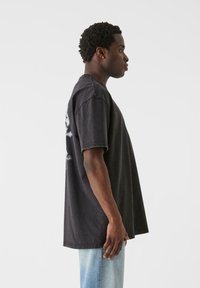 Oversized sort bomulds t-shirt med korte ærmer, rund halsudskæring, med grafiske detaljer på ryggen, stylet med lyseblå jeans.