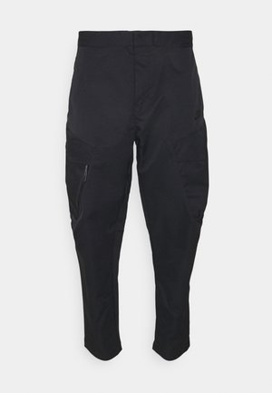 Czarne sportowe spodnie Nike z kieszenią na zamek na lewej udzie i zwężanymi nogawkami na białym tle.