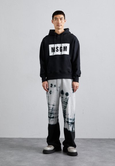 Schwarzer Hoodie mit weißem "MSGM"-Logo, kombiniert mit grauen Batik-Sweatpants mit schwarzen Akzenten und klobigen grauen Sneakers.