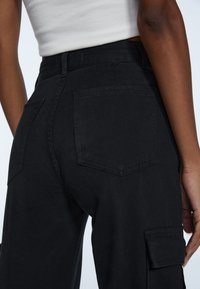 Zwarte katoenen cargobroek met een aangesloten taille, achterzakken en details op zijzakken, met een soepele textuur en strakke lijnen.