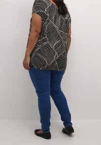 Haut à motifs noir et beige avec une coupe ample et des manches courtes, associé à un jean bleu ajusté et des chaussures plates noires.