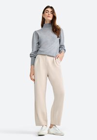 Grijze coltrui met uitlopende mouwen, gecombineerd met beige wijde broek en witte sneakers. Glad textuur, modern design.