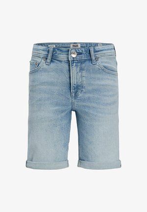 Fiú áll, sötétkék csíkos galléros pólót, világos farmer rövidnadrágot, fehér zoknit és bézs fűzős cipőt visel, mosolyog a kamerába.