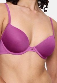Lilla polstret bh med justerbare stropper, en glat tekstur og lukning foran med hægte. Har en skinnende detalje.