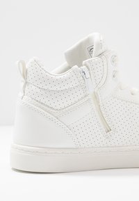 Weißer Hochschnitt-Sneaker mit perforierten Details, seitlichem Reißverschluss, Schnürung, gepolstertem Kragen und Schlaufe auf einem weißen Hintergrund.