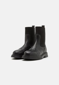 Bottines en cuir noir avec panneaux latéraux élastiques, bout rond et semelle en caoutchouc texturée. Équipées de languettes pour un enfilage facile.
