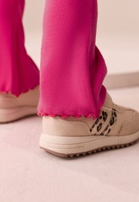 Rosa ribbade byxor med en vågig fåll, kombinerade med beiga sneakers med leopardmönstrad detalj och texturerad mockayta.