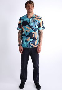 Chemise à manches courtes à boutons avec un motif abstrait bleu, orange et marine ; elle dispose d'une petite poche poitrine et d'une coupe décontractée.