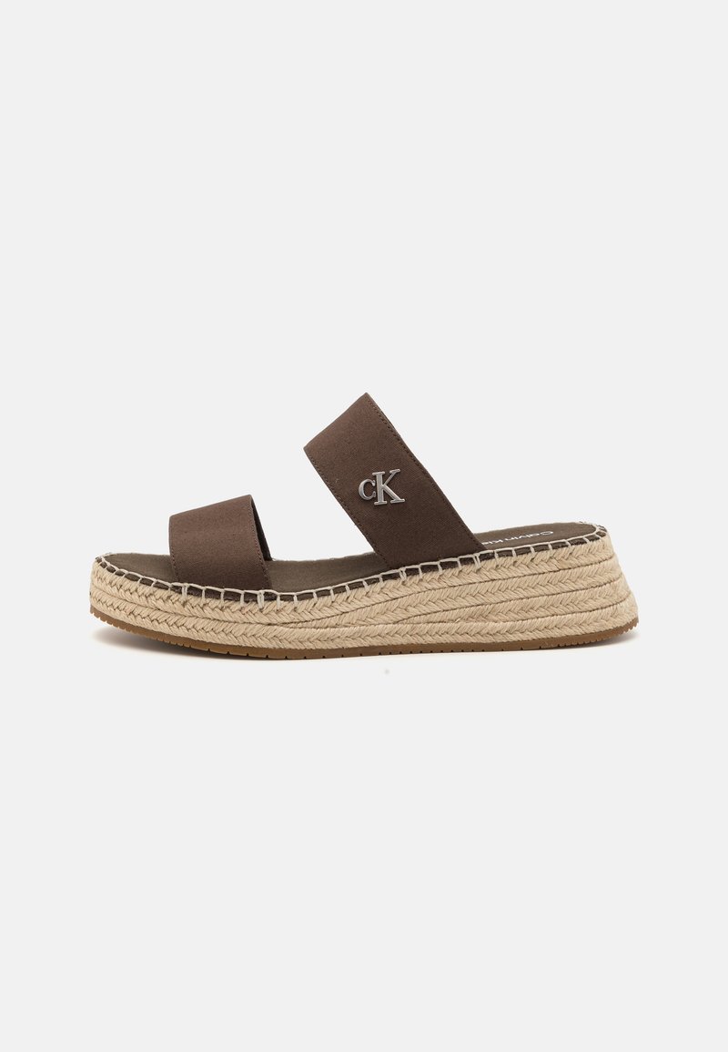 Brūni zābaci ar divām auduma siksnām, ar jūtu detaļu ap zoli un logotipa akcentu sānos. Plakana gumijas zole.