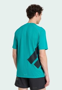 Turkos träningsskjorta med ett texturerat mönster, med en stor svart geometrisk design på baksidan och korta ärmar.