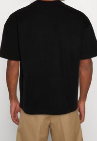 Sort bomulds t-shirt med korte ærmer og en afslappet pasform. Viser en ensfarvet ryg uden grafik eller dekorationer, med en sømløs halsudskæring.